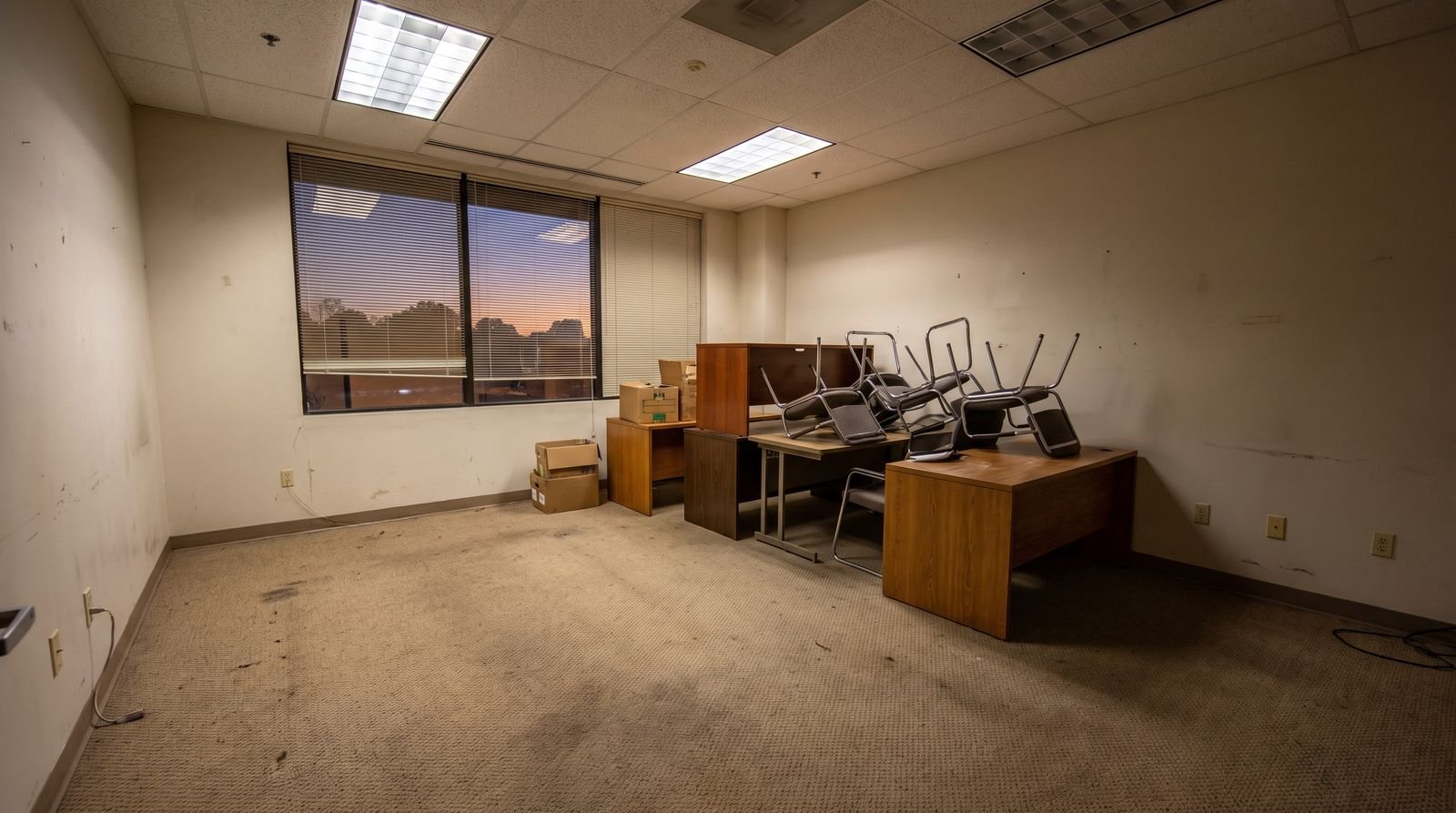 An office being cleared, desks and stacked chairs pushed to one side